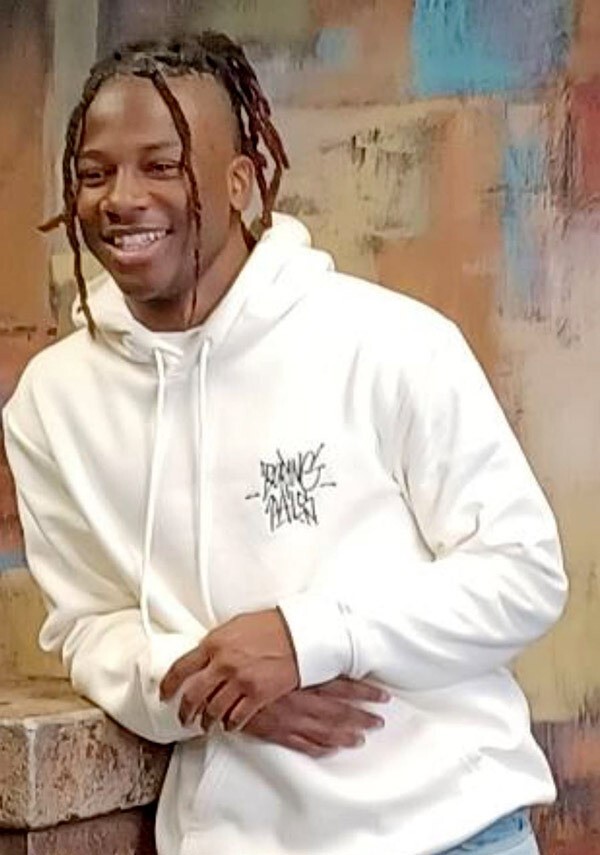 A young man poses against a brick wall and is smiling.